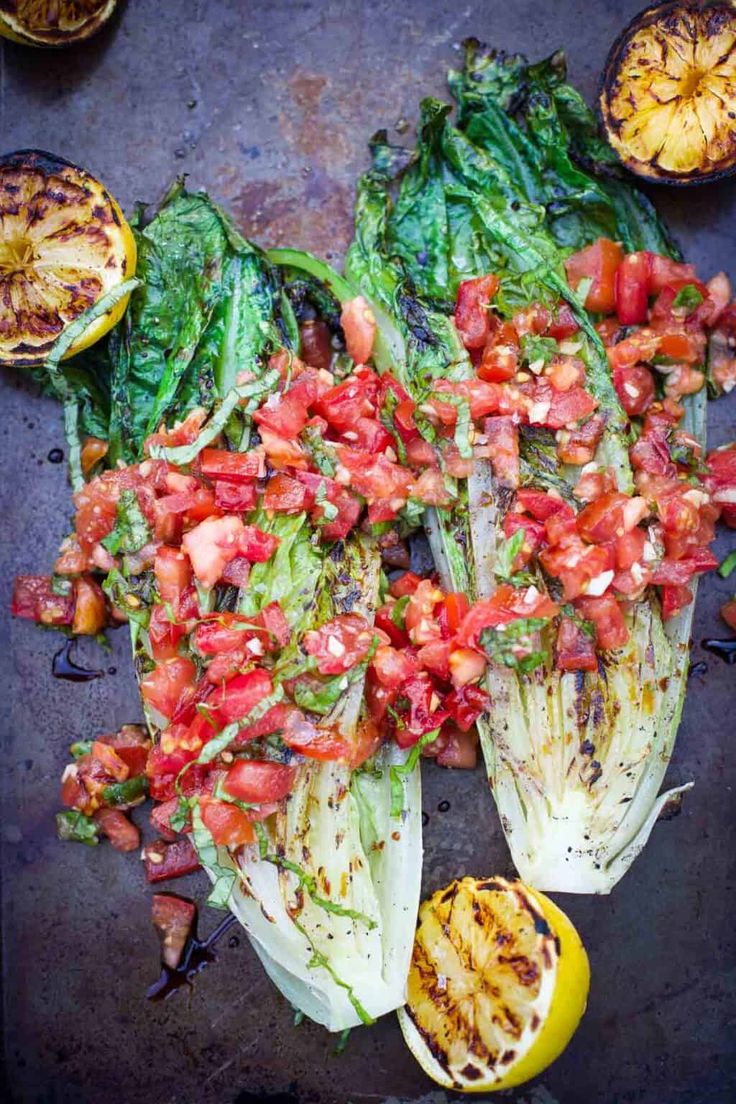 grilled cabbage with tomatoes and avocado on a baking sheet next to lemons