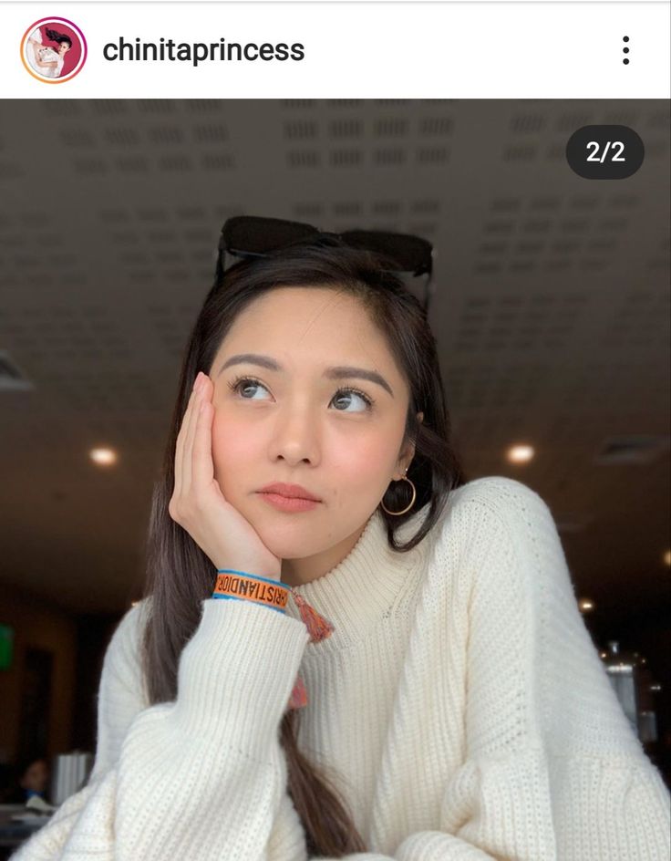 a woman with her hand on her chin and looking at the camera while wearing a white sweater