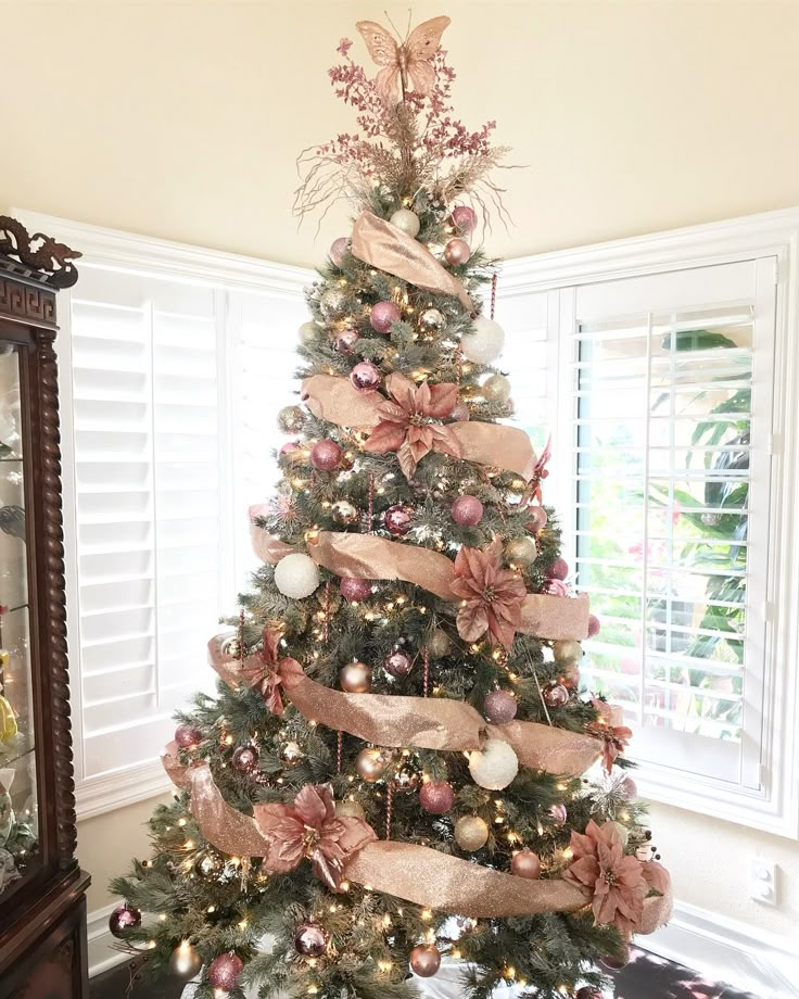 a decorated christmas tree with pink and gold ribbons on it in front of a window