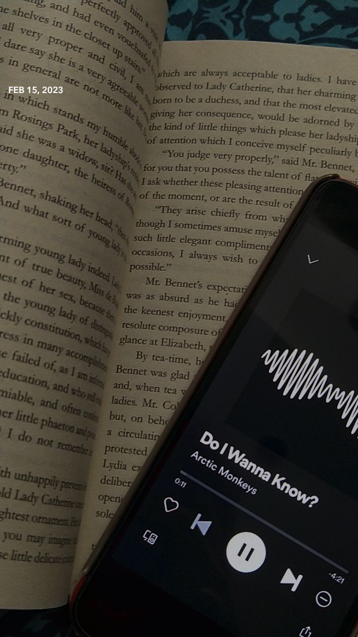 an open book with music playing on it next to a cell phone and headphones