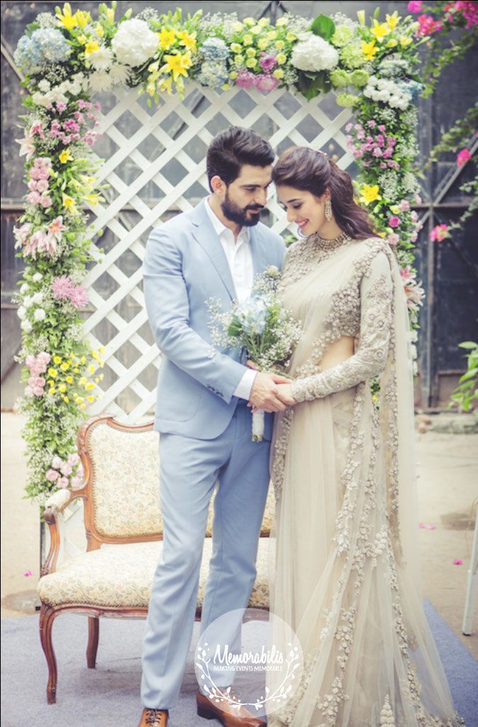 a man and woman standing next to each other in front of a flower covered arch