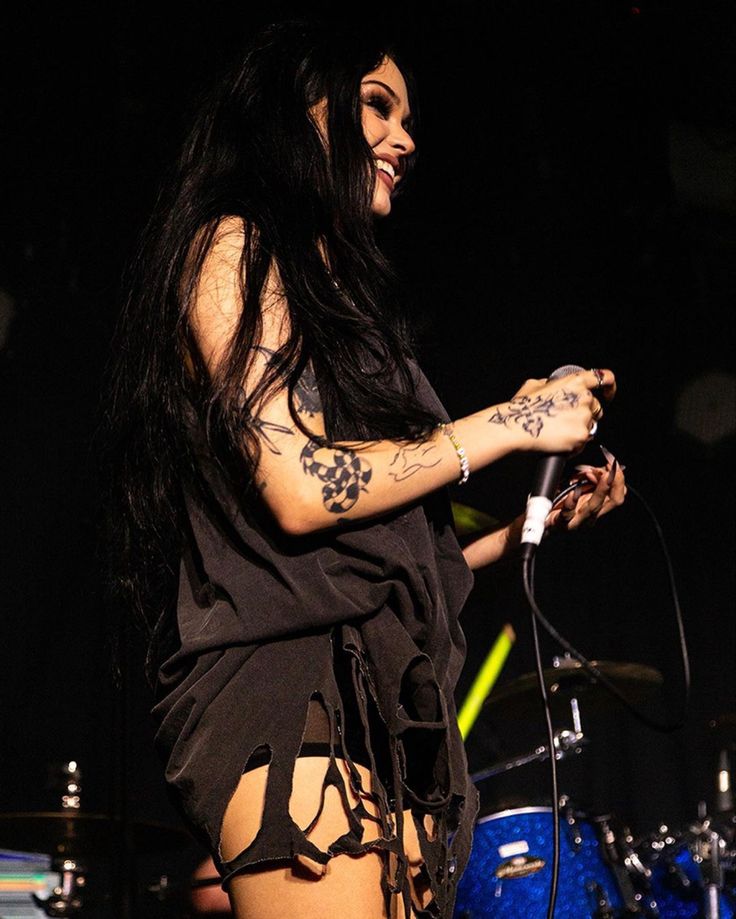 a woman with long black hair and tattoos on her body standing in front of a drum set