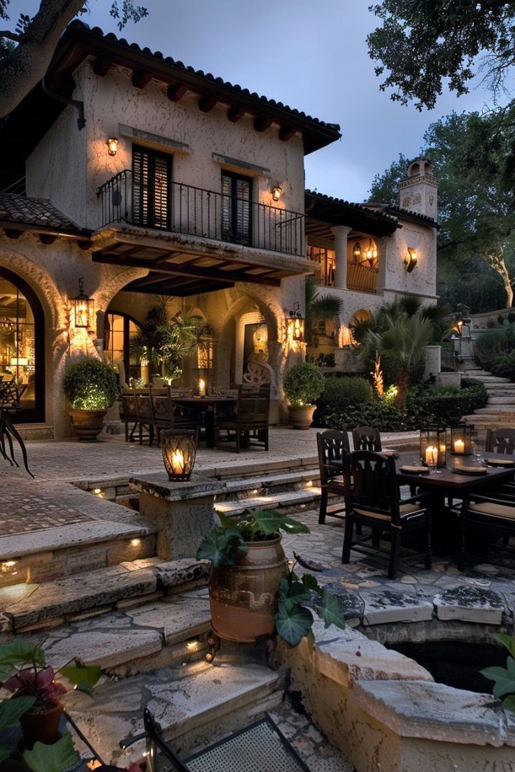 an outdoor dining area in front of a large house with stone steps leading up to it