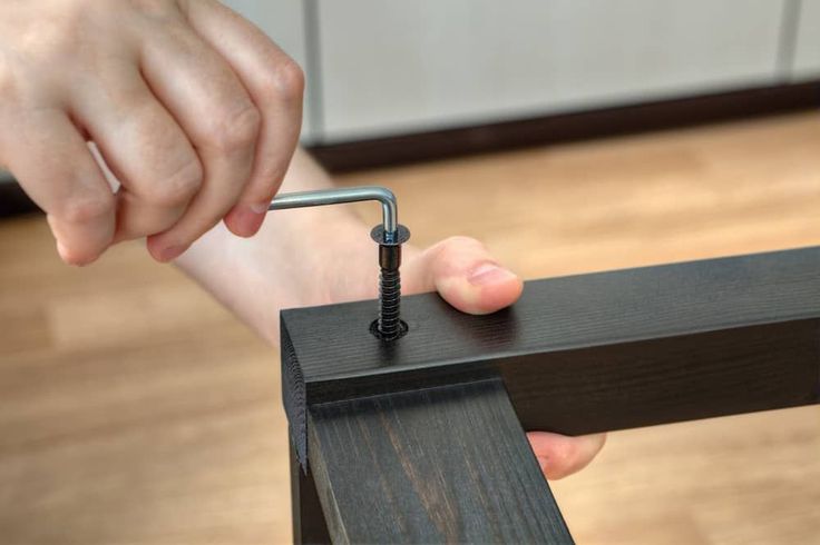 a person holding a screw in their right hand while working on a piece of wood