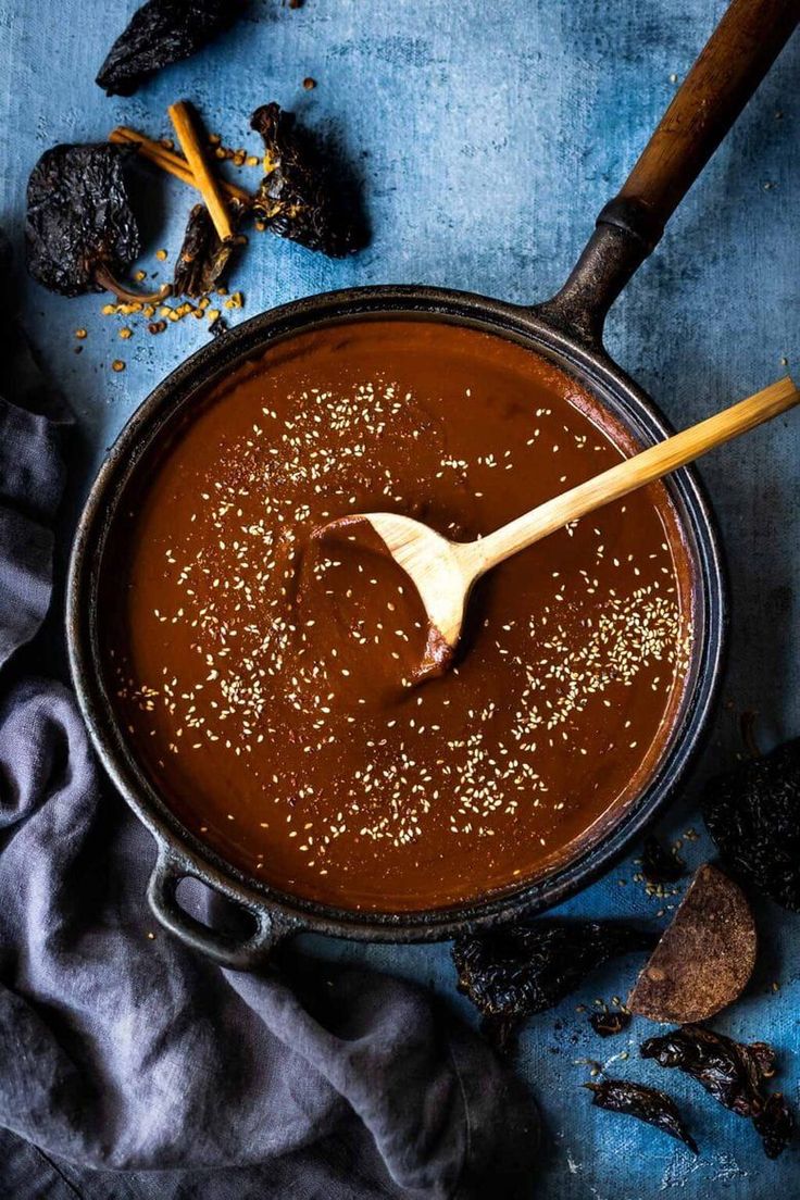 a wooden spoon in a pot filled with brown liquid and spices on a blue surface