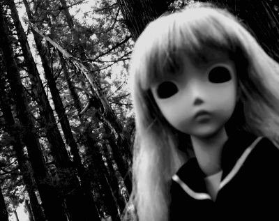 a black and white photo of a doll with long blonde hair in front of trees