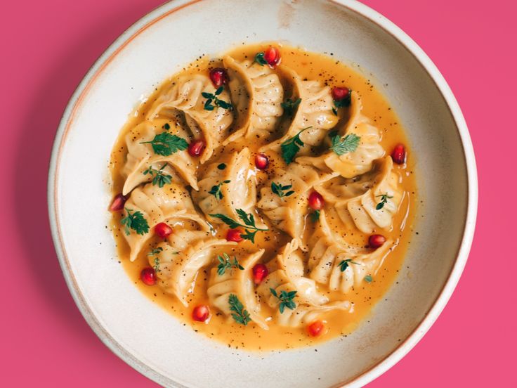 a white bowl filled with dumplings covered in sauce and garnished with parsley