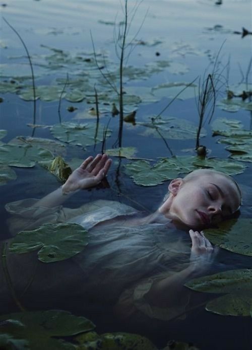 a woman floating in water with lily pads on her body and head above the water's surface