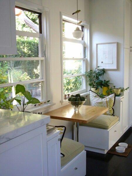 a kitchen with white walls and wooden table surrounded by potted plants on the windowsill