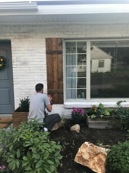 a man kneeling down in front of a house next to some plants and flowers on the ground