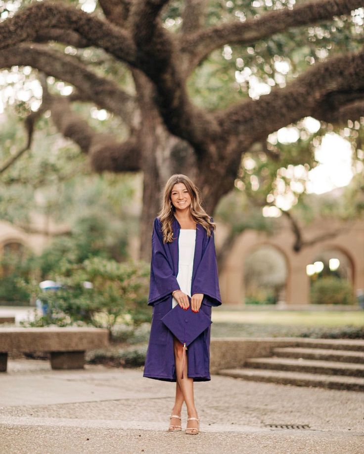 a woman standing in front of a large tree wearing a purple coat and white dress