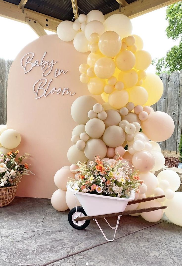 a baby shower with balloons, flowers and a wheelbarrow in front of it