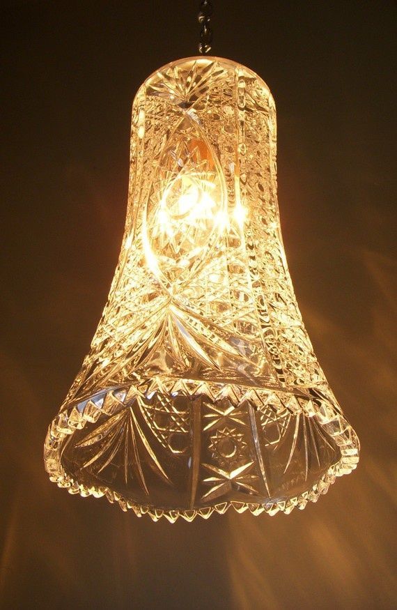 a glass lamp hanging from the ceiling in front of a dark background with light coming through it