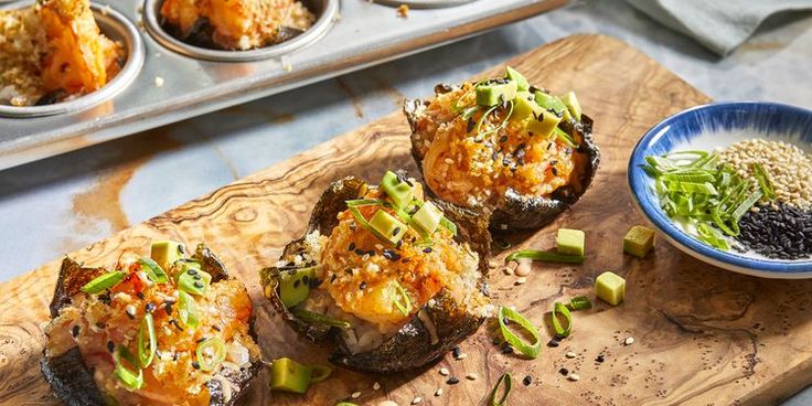 baked stuffed mushrooms on a wooden cutting board next to a bowl of black sesame seeds