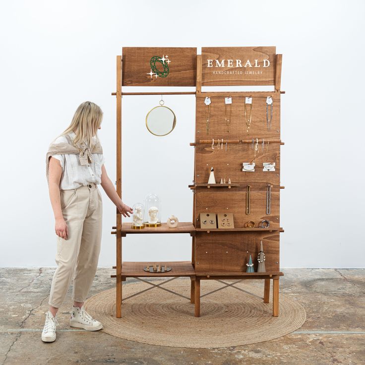 a woman standing in front of a wooden jewelry stand