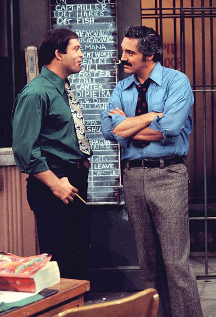 two men standing next to each other in front of a chalkboard with writing on it