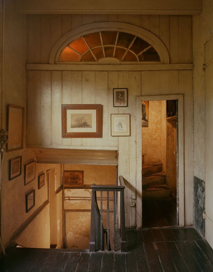 an empty room with pictures on the wall and stairs leading to another room in the house