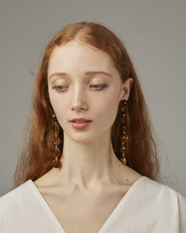 a woman with red hair wearing earrings and a white shirt is looking at the camera