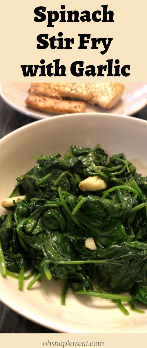 spinach stir fry with garlic in a white bowl on a table next to bread