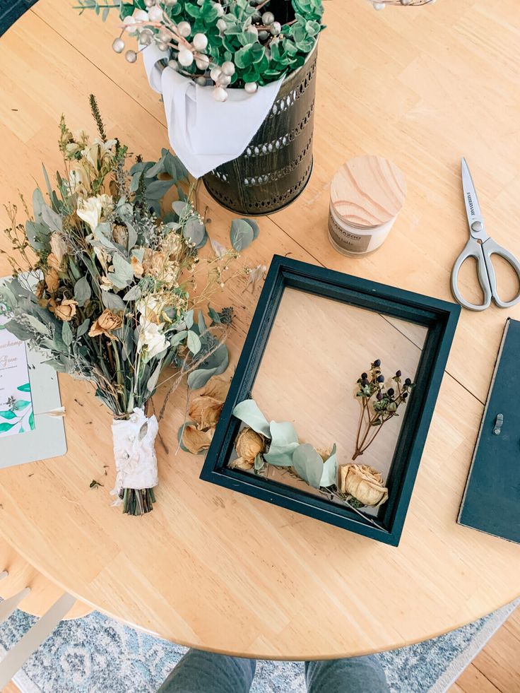 a table topped with flowers and framed pictures next to a pair of scissors on top of a wooden table