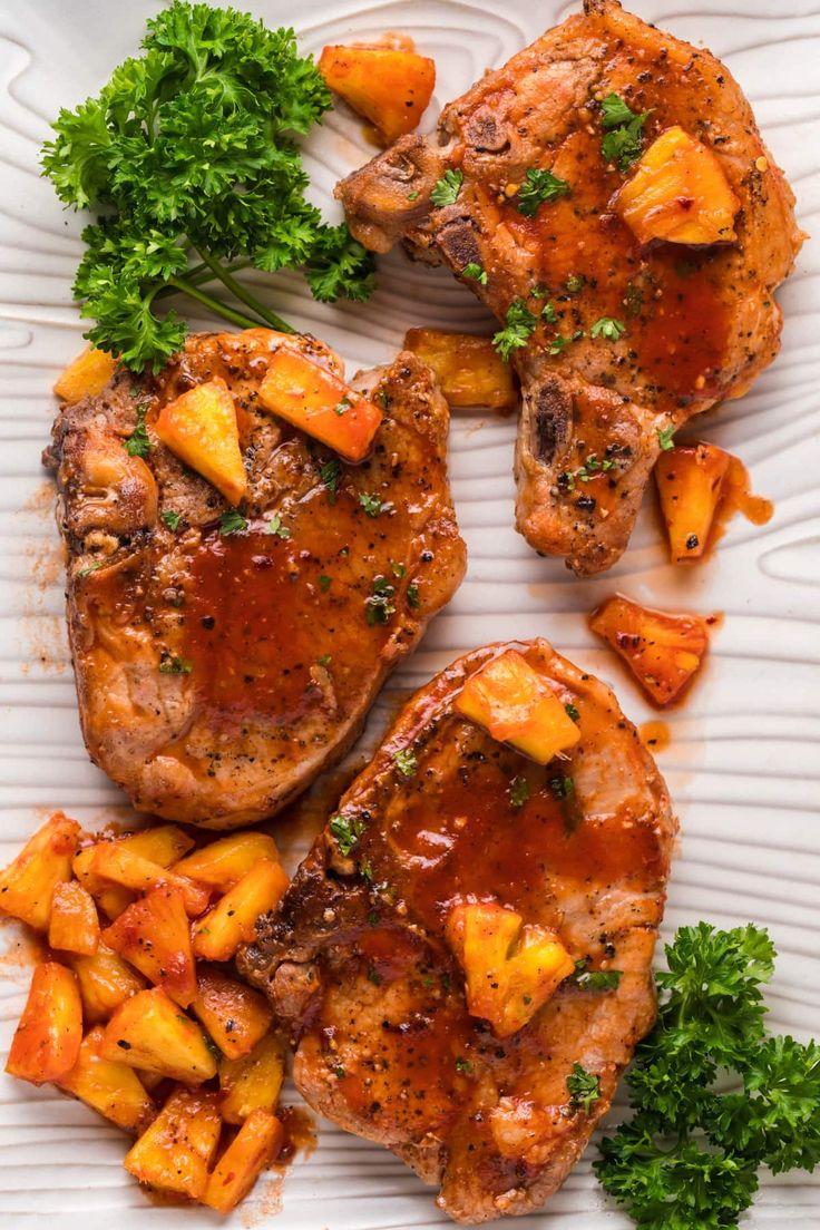 two pieces of meat with pineapples and parsley on a white platter