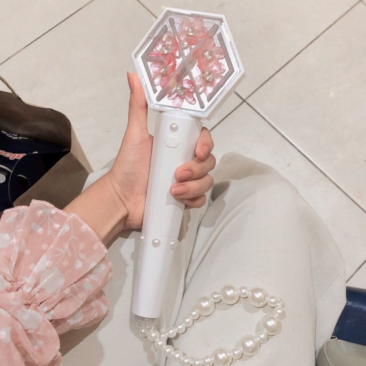 a person holding a white object with pink flowers in it's center and pearls on the bottom