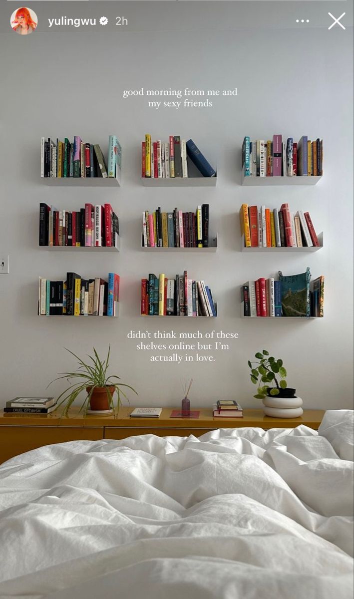 there is a bed with white sheets and books on the shelves above it that are filled with books