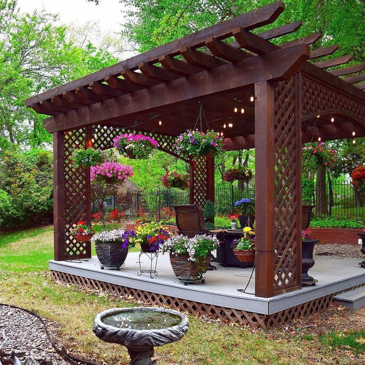 an outdoor gazebo with potted plants and flowers on the ground next to it