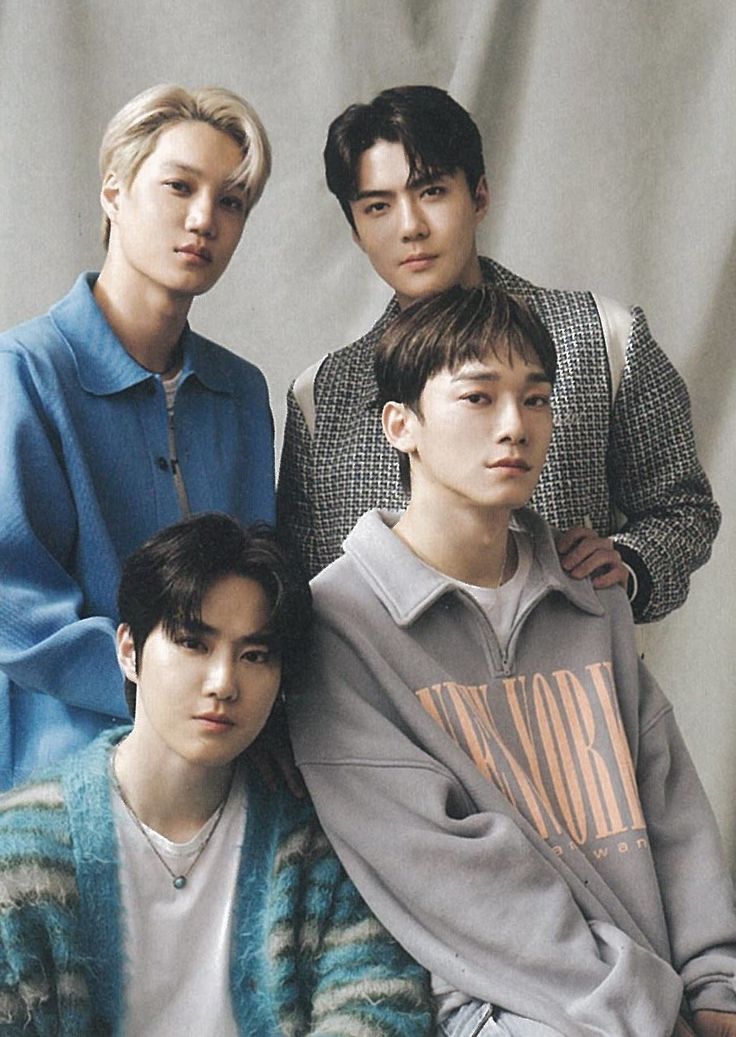 four young men are posing for a photo in front of a white background, one is wearing a blue sweater and the other wears a gray shirt