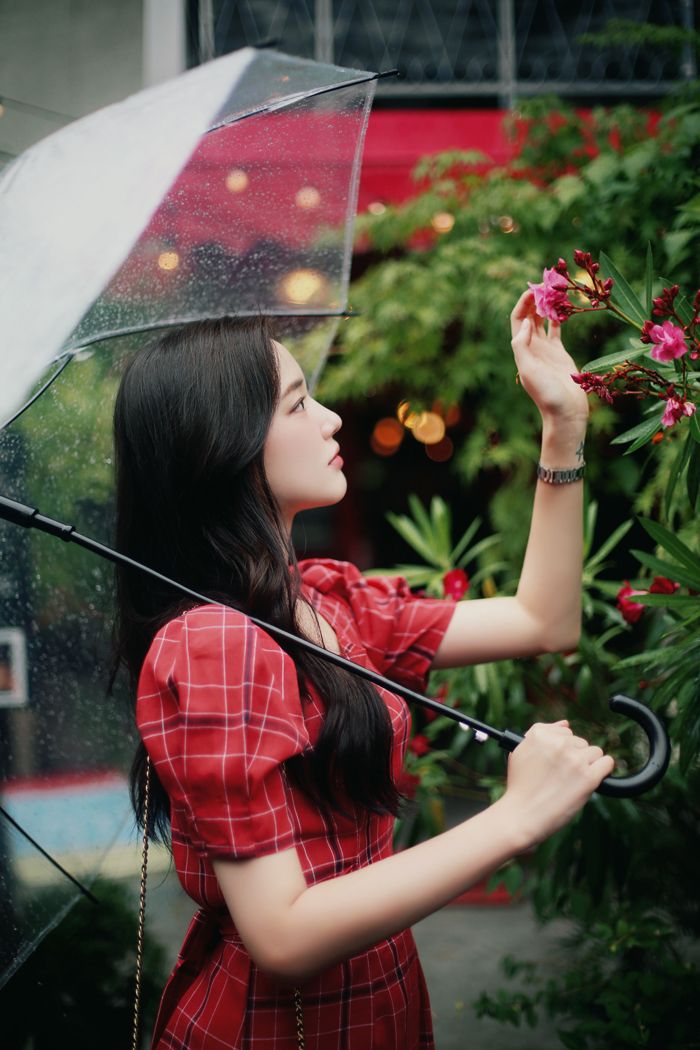 a woman in a red dress holding an umbrella over her head and looking at flowers