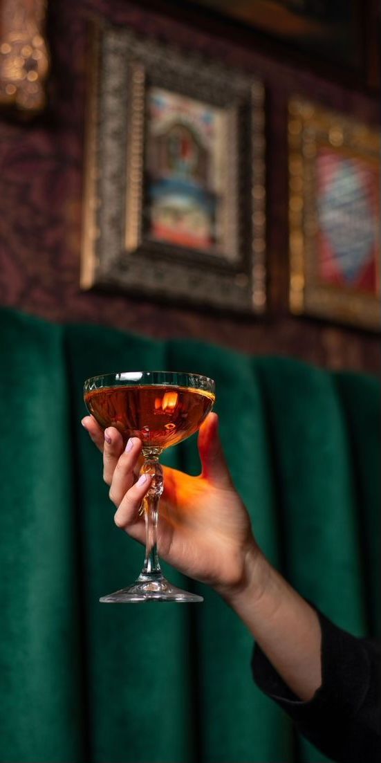 a person holding up a wine glass in front of a green wall