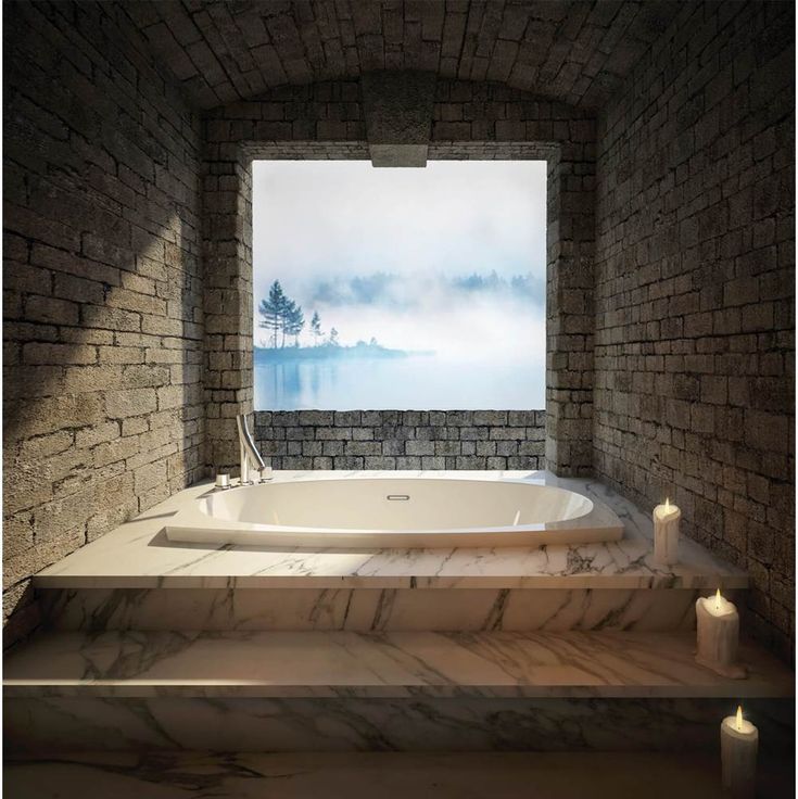 a bath tub sitting next to a window in a stone walled room with candles on the floor