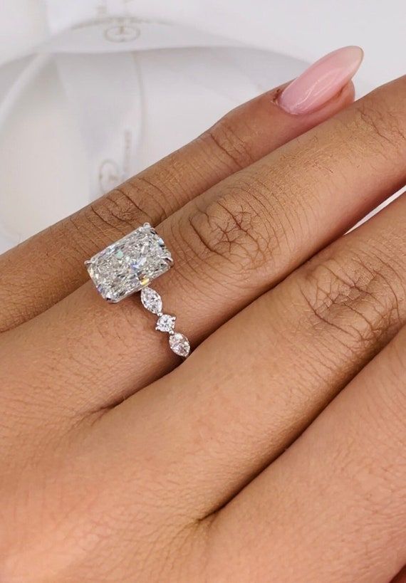 a woman's hand with a diamond ring on top of her finger and the other hand holding an engagement ring