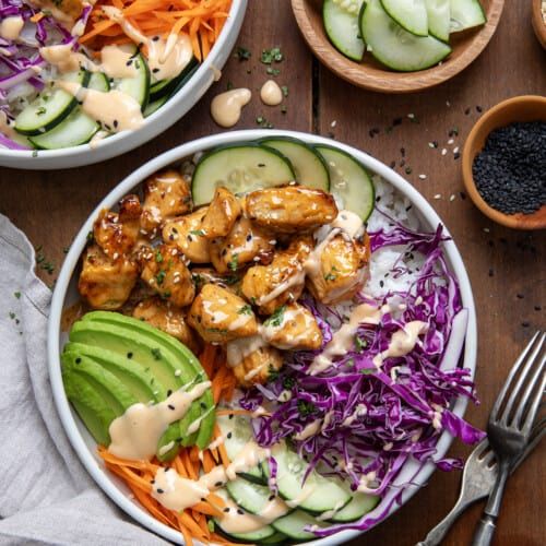 two bowls filled with chicken and veggies on top of a wooden table next to silverware