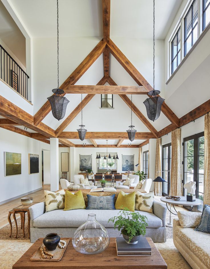 a living room filled with lots of furniture next to tall windows and wooden ceiling beams