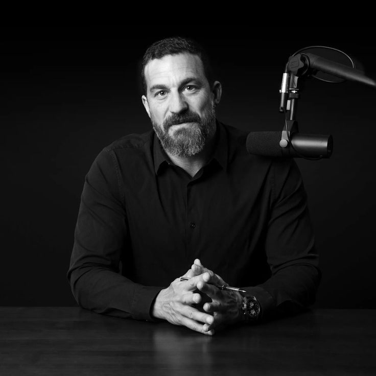 a man sitting at a table in front of a microphone with his hands folded out