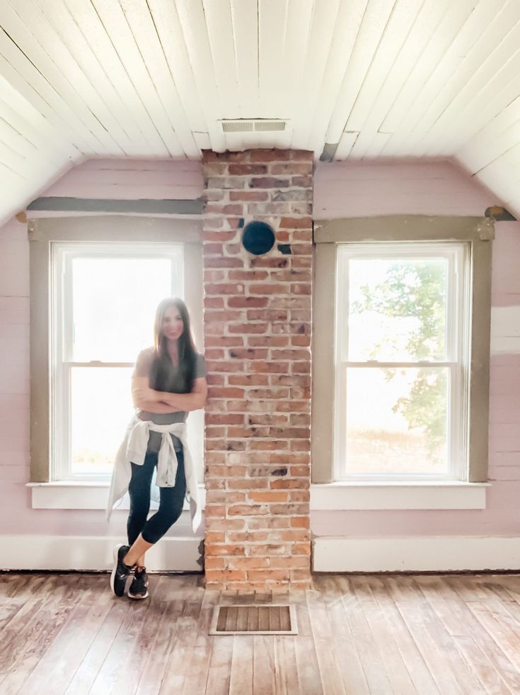 a woman leaning against a brick wall in a room with hardwood floors and pink walls