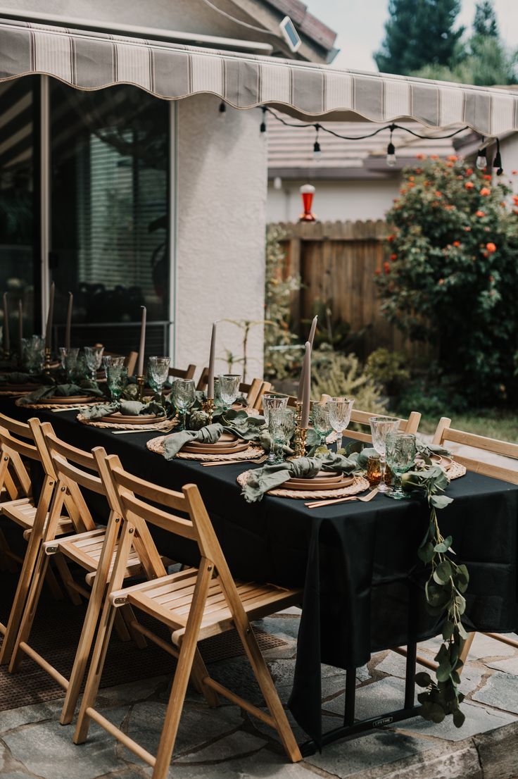 an outdoor dining table set up with black linens and greenery on the tables