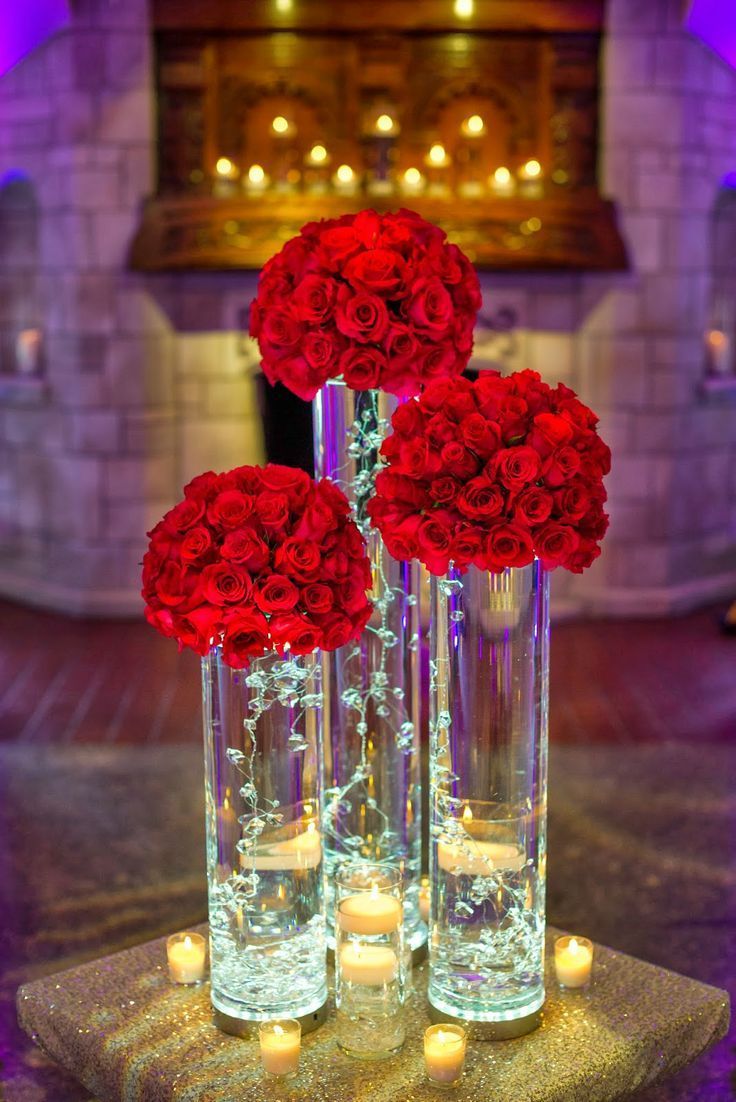 three tall vases filled with red roses on top of a table next to candles