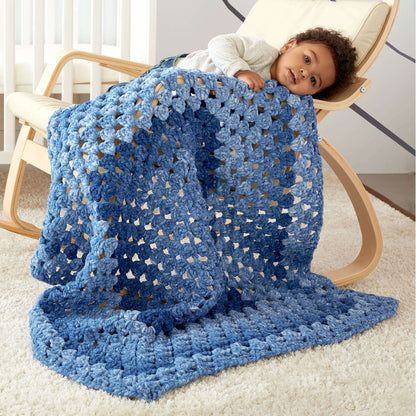 a baby laying on top of a blue crocheted blanket next to a rocking chair