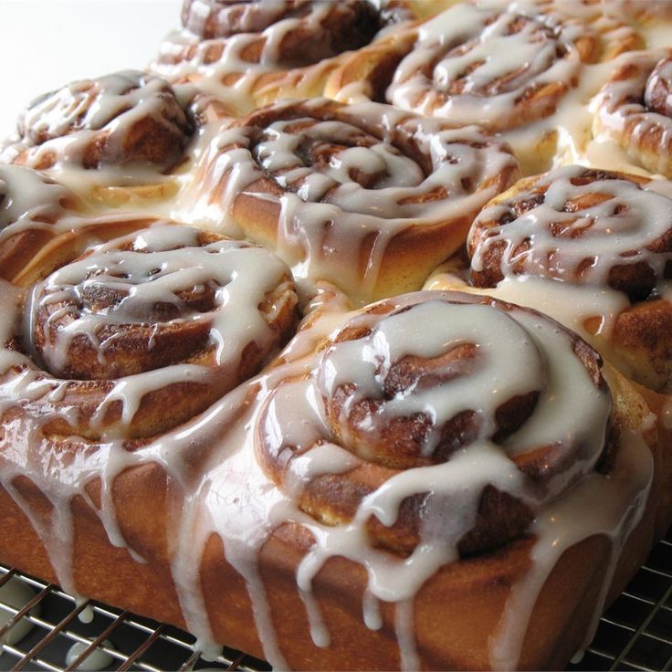 cinnamon rolls with icing sitting on top of a cooling rack