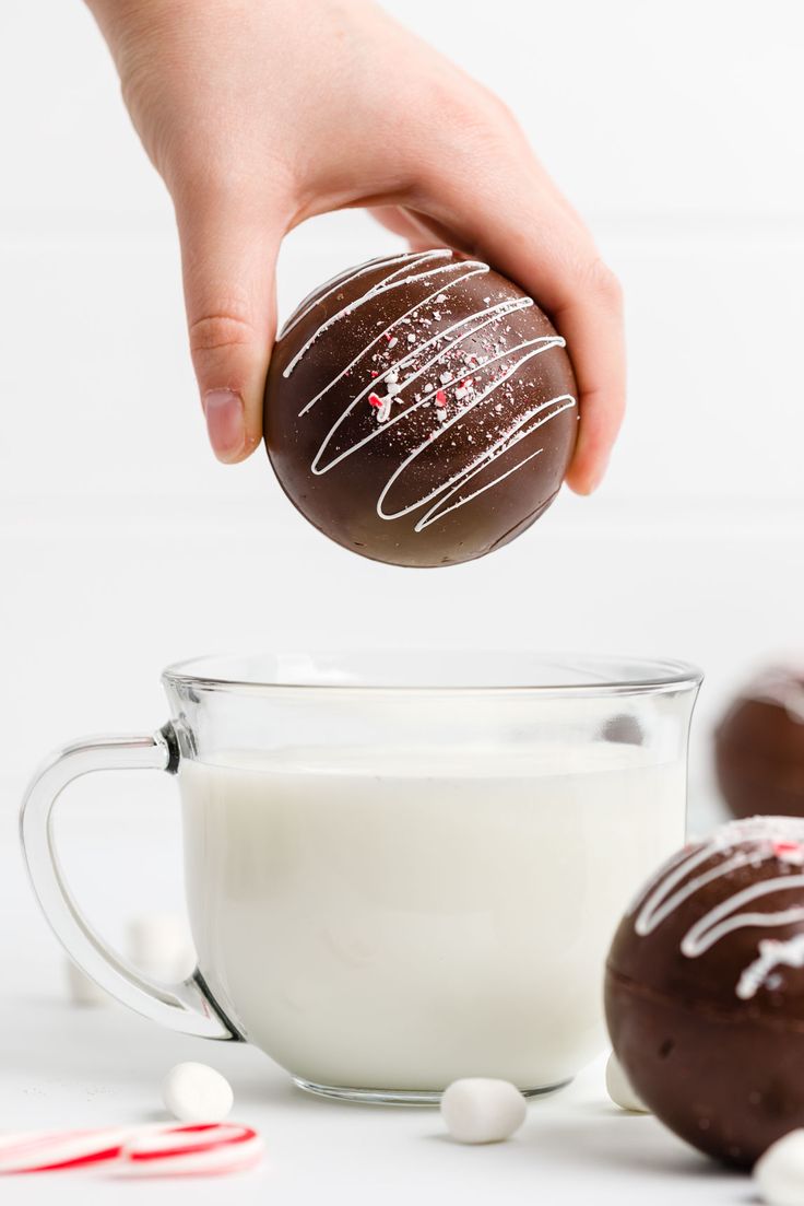 a person is dipping chocolate into a bowl of milk with marshmallows and candy canes in the background