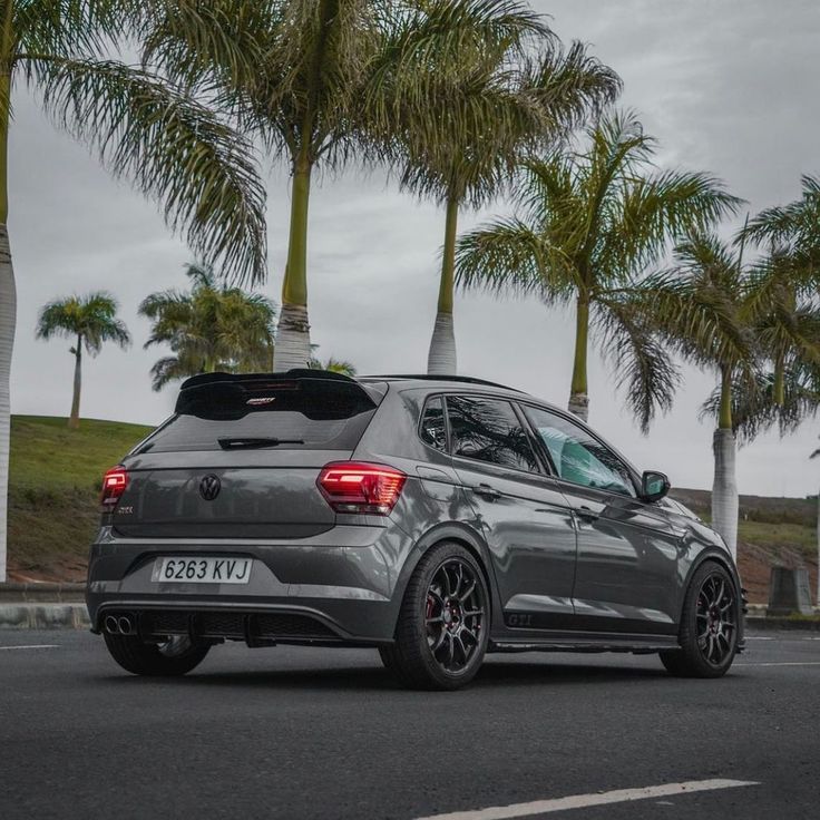 the rear end of a gray volkswagen car parked in front of palm trees