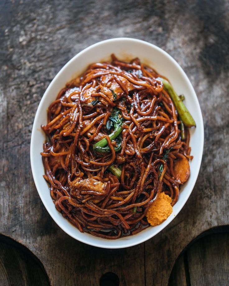 a bowl filled with noodles and vegetables on top of a wooden table next to a fork