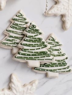 christmas cookies decorated with green and white icing on a marble countertop next to ornaments