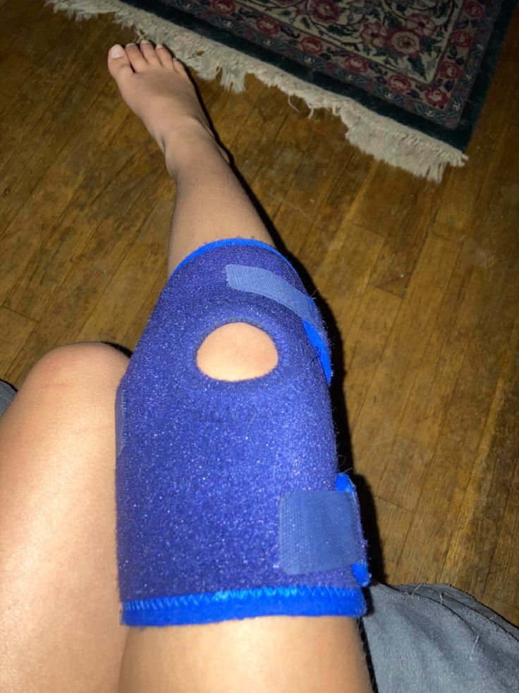 a person with a cast on their leg wearing a blue knee brace and sitting on the floor