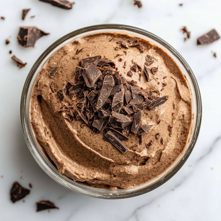 a glass bowl filled with chocolate pudding on top of a white countertop next to pieces of chocolate