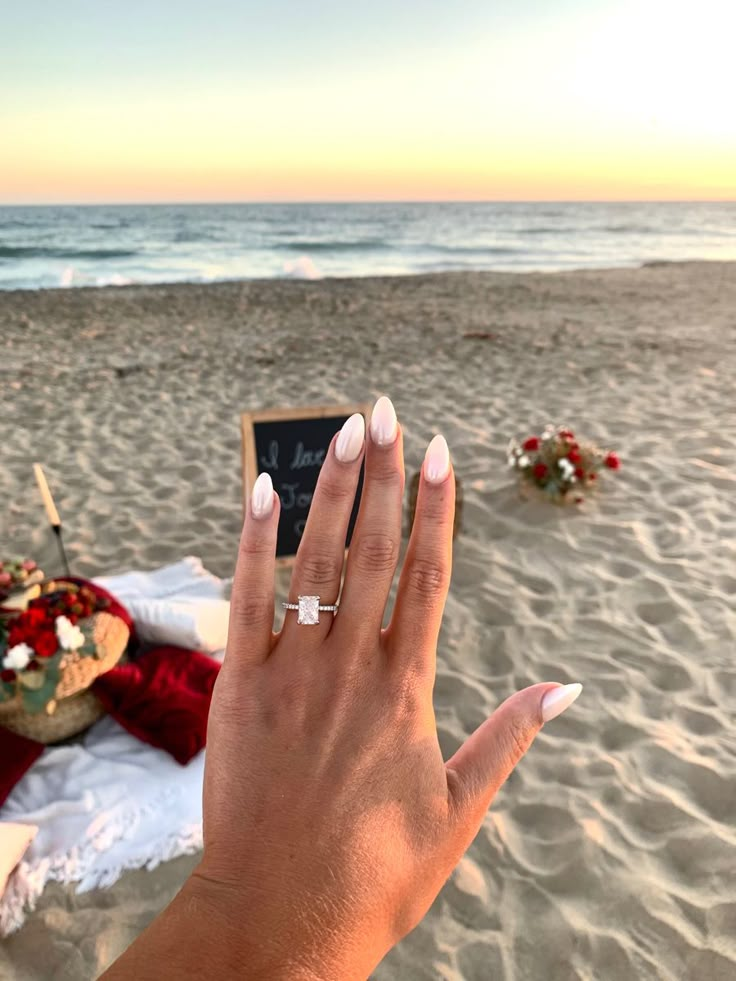 a woman's hand on the beach with an engagement ring in front of her