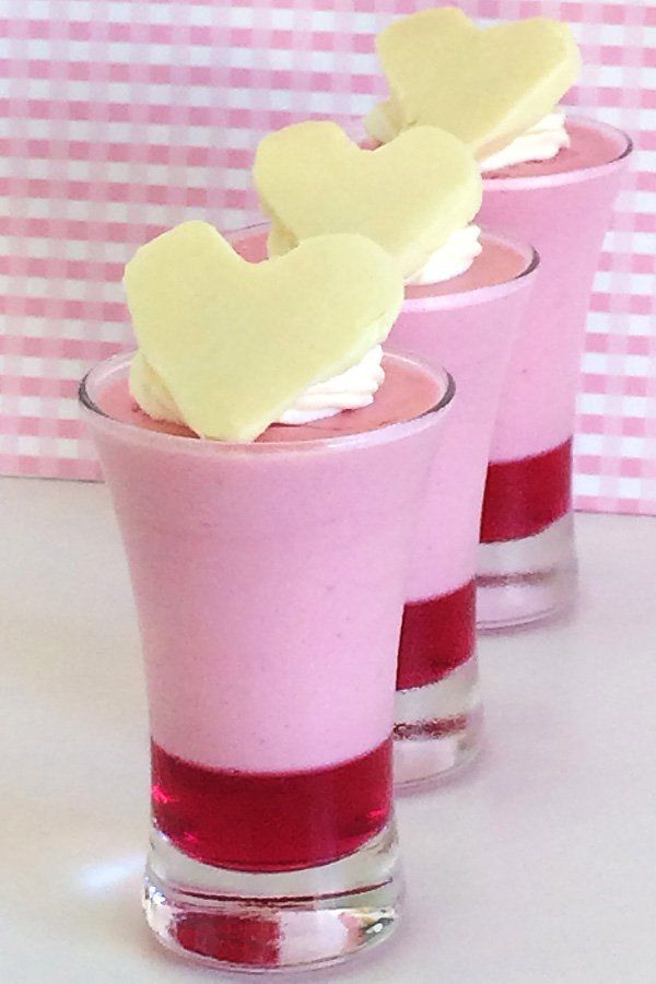 three desserts in small glasses with hearts on the top one is pink and white