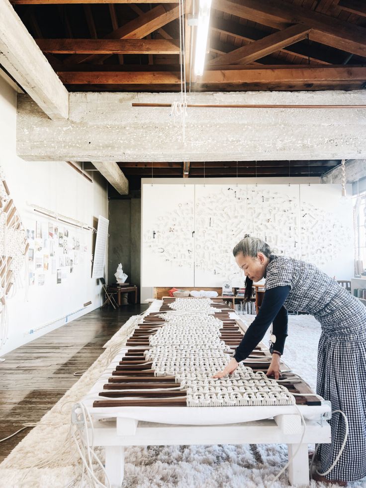 a woman is working on an art piece in the middle of a room with white walls and wood beams